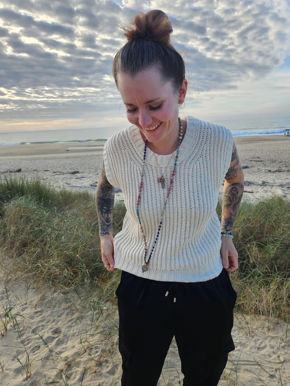 Lachende Frau am Strand mit Mala-Kette und Tattoos – Ausdruck von Lebensfreude, Erdung und Freiheit