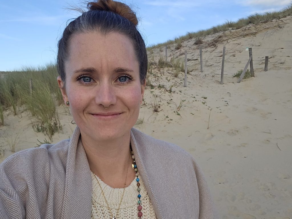 Frau mit sanftem Lächeln vor einer natürlichen Dünenlandschaft – Ausdruck von innerer Ruhe, Weite und Herzensverbundenheit